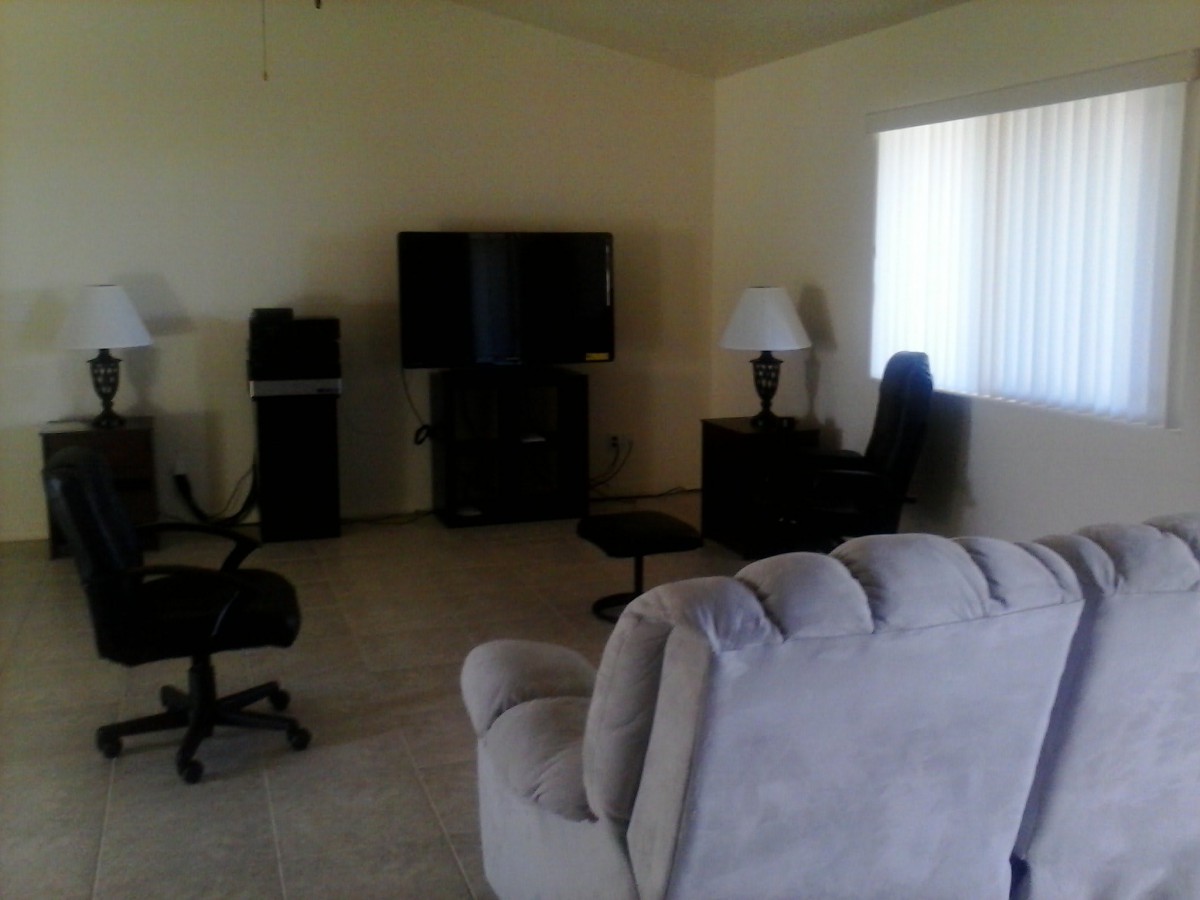 A cozy living room with a television, sofa, chairs, and a lamp.