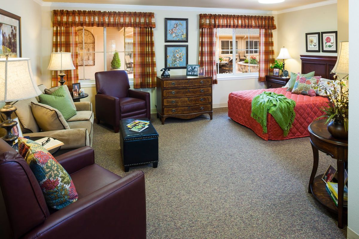 A cozy bedroom with warm decor, featuring a bed, armchairs, and a dresser.
