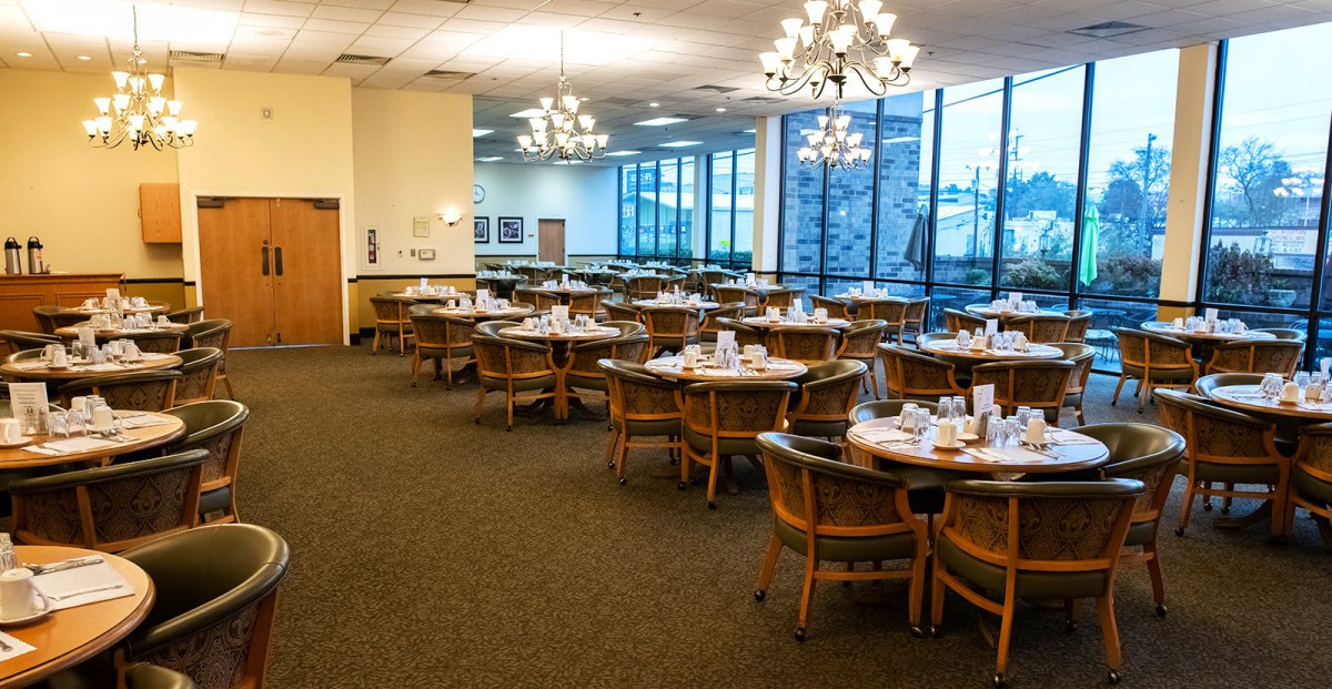 A spacious banquet hall is elegantly set up with round tables and chairs, ready for an event.
