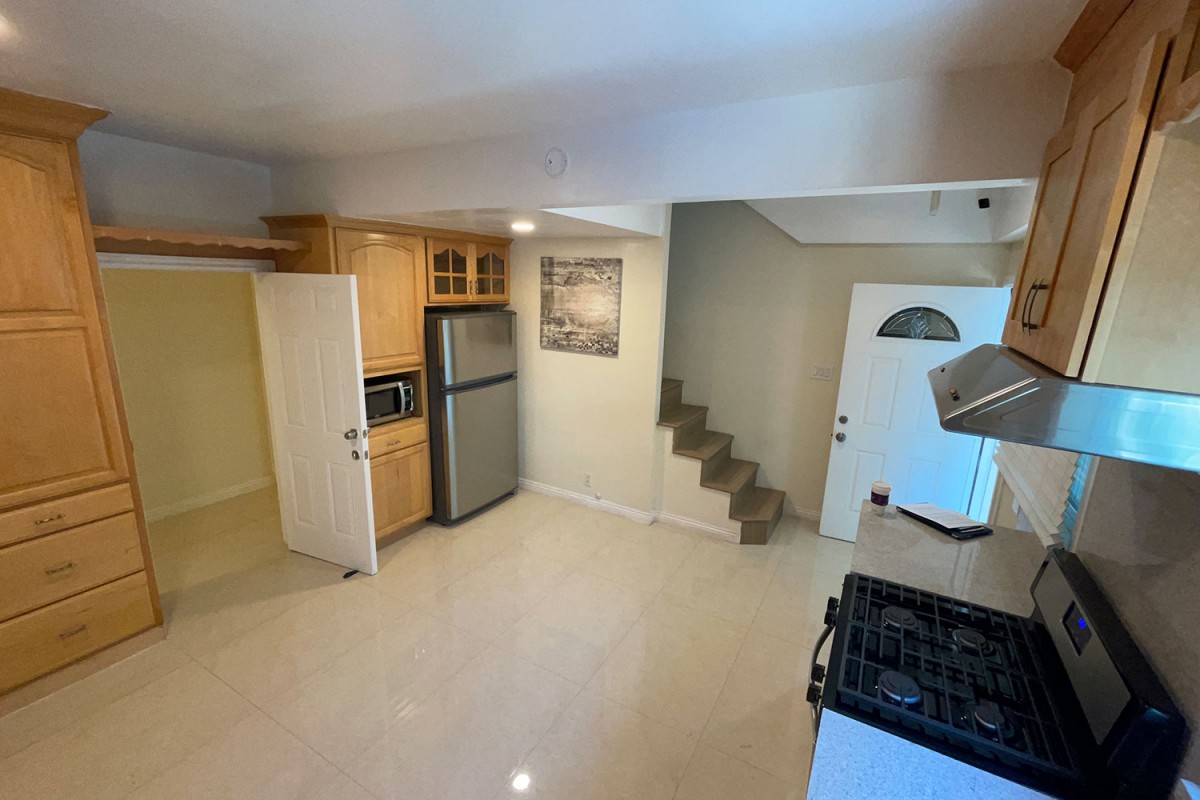 A modern kitchen with wooden cabinets, appliances including a fridge and microwave, and an adjacent staircase.