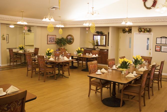 A well-lit dining room interior with neatly arranged tables and chairs, adorned with decorative plants.