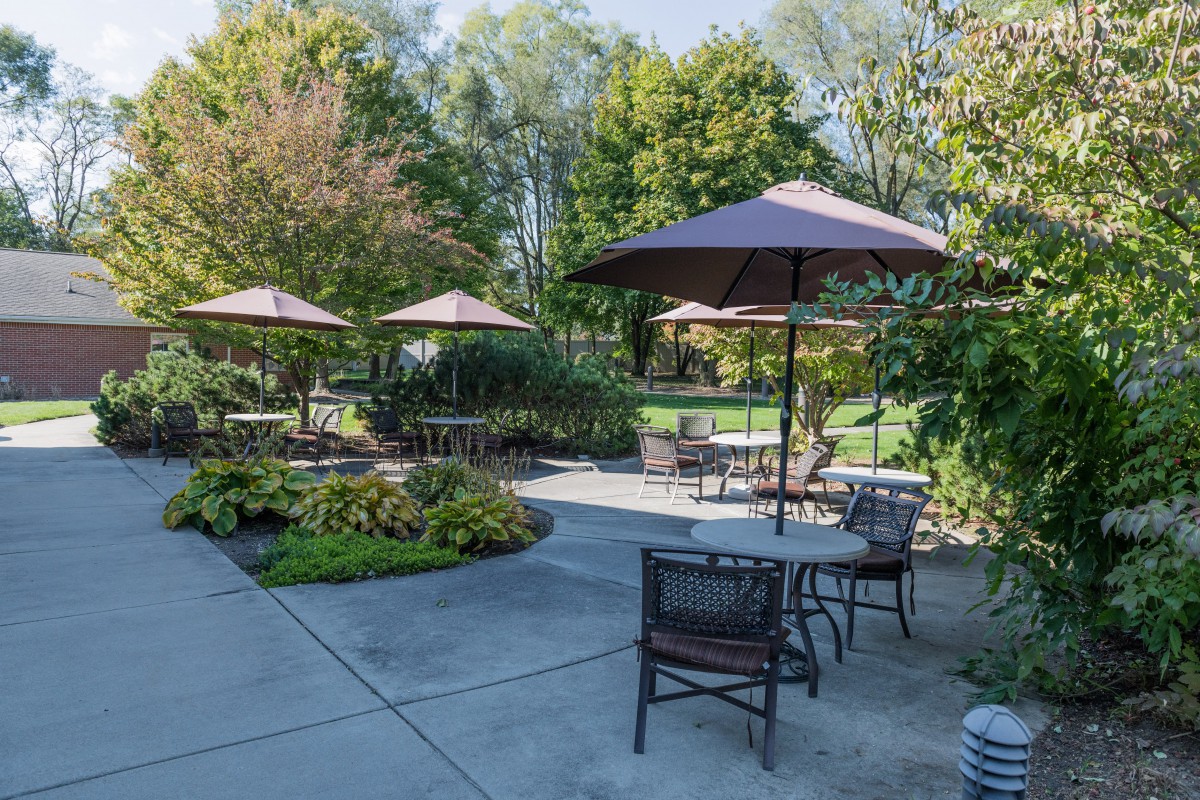 A sunny outdoor patio with tables, chairs, and umbrellas surrounded by lush greenery.