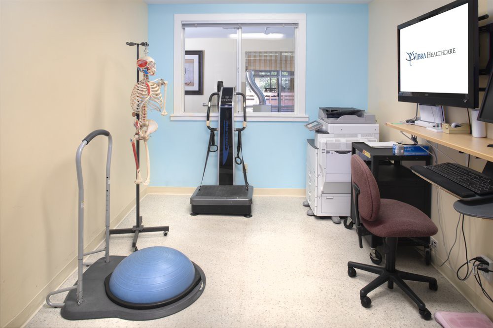 A small office space featuring exercise equipment, a medical skeleton model, and an office setup with a printer and desk.