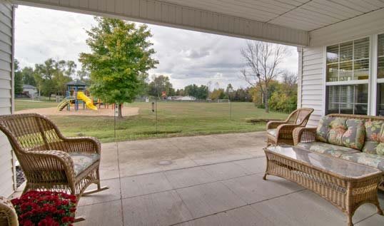 A cozy patio with wicker chairs overlooks a lush lawn and playground.
