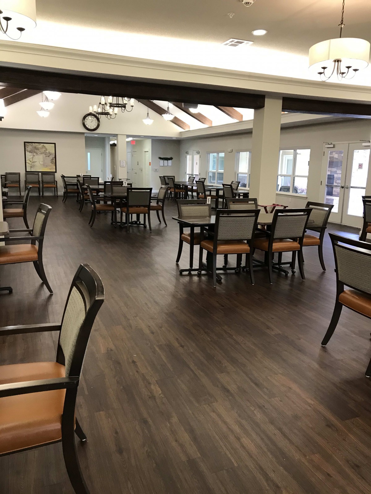 An empty dining room with wooden floors and neatly arranged tables and chairs.