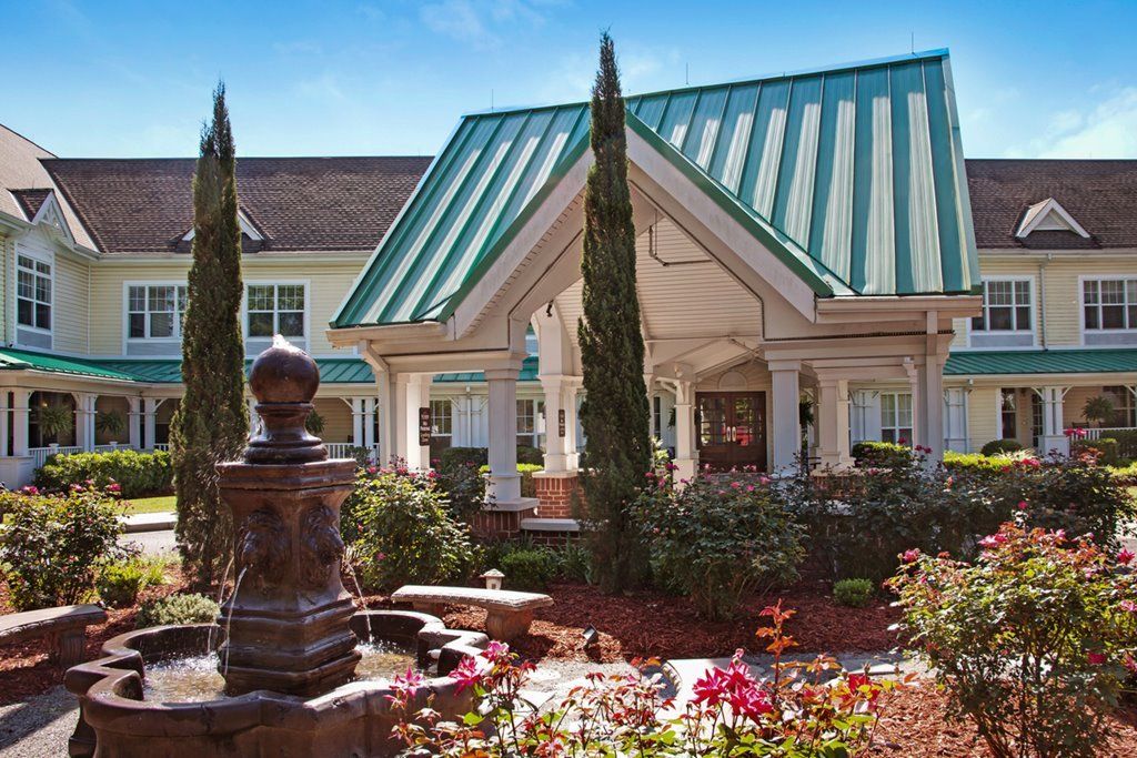 A beautifully landscaped entrance featuring a fountain and garden in front of a building with a green metal roof.