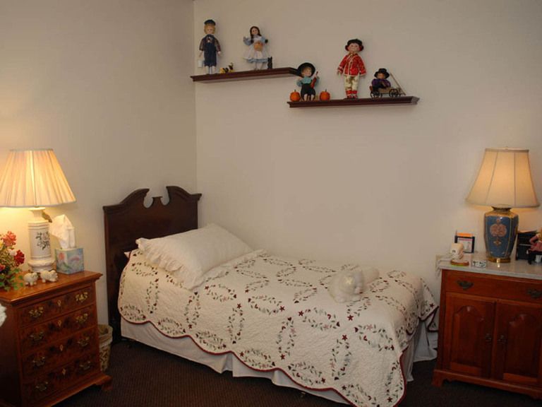 A cozy bedroom with a vintage quilt on the bed and shelves displaying decorative dolls.
