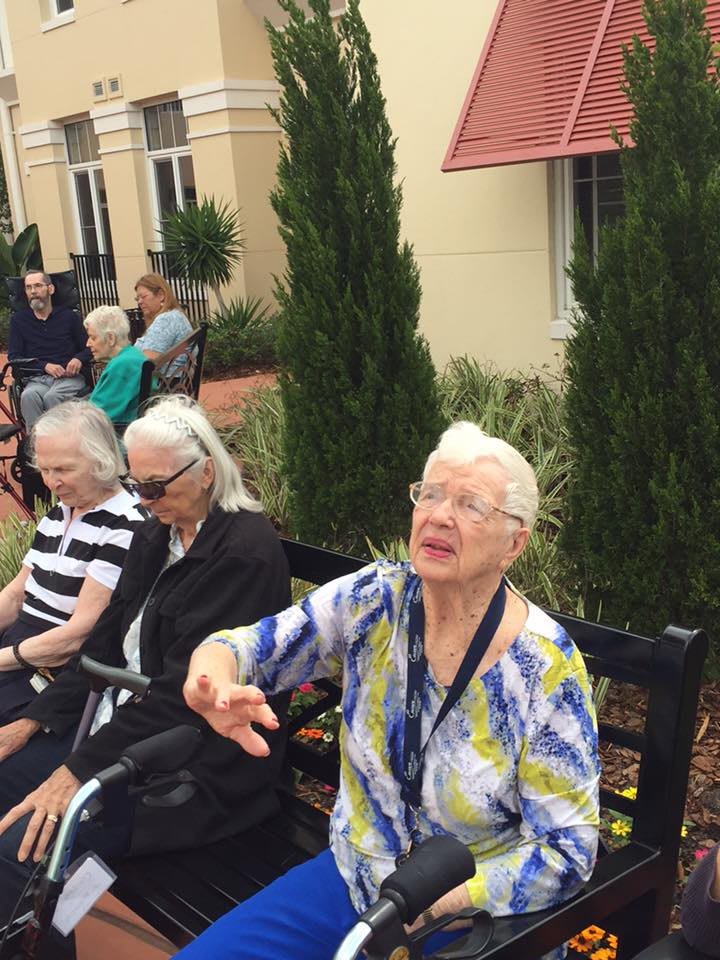 A group of elderly people sitting on a bench outdoors, enjoying a social gathering.