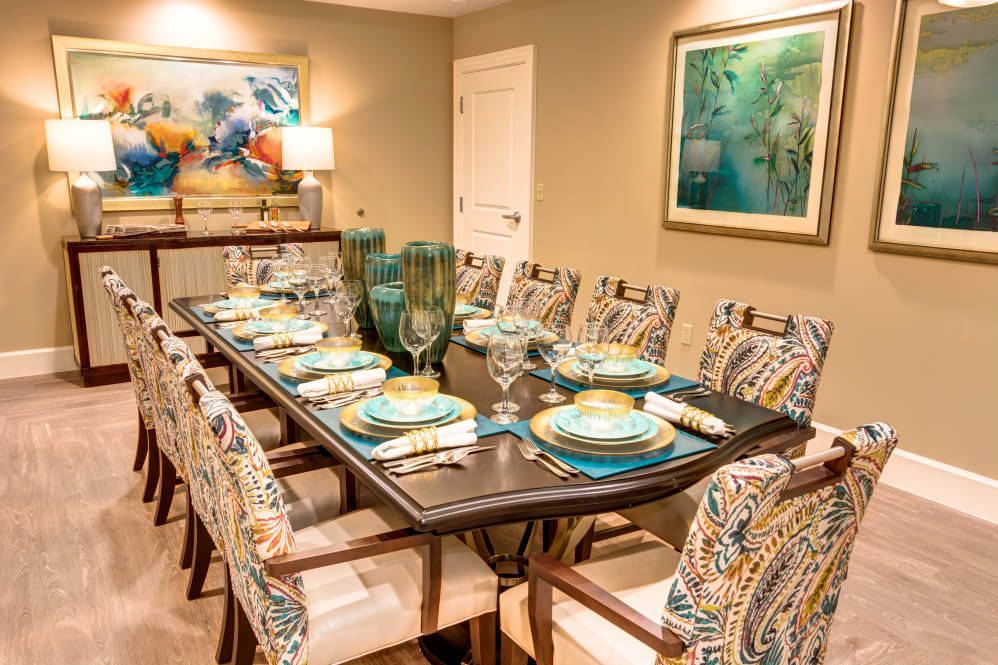 A well-decorated dining room featuring a large table set for a meal, with vibrant artwork on the walls and elegant glassware.
