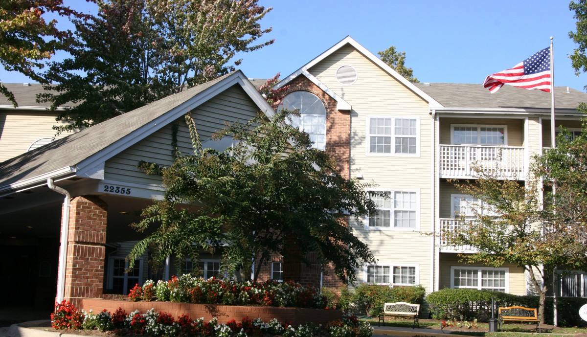 A view of a residential apartment building surrounded by trees and landscaping on a sunny day.
