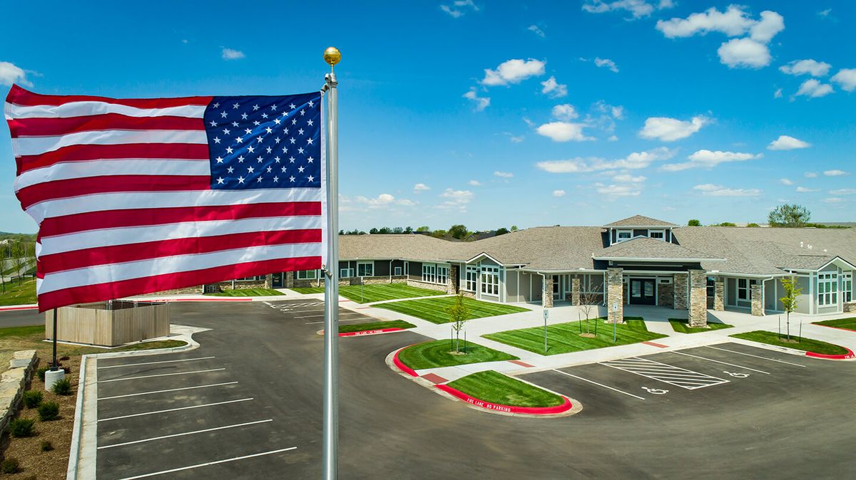 A view of a building with an American flag and a spacious parking lot under a partly cloudy sky.