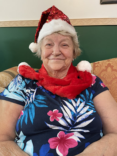 An elderly woman celebrates the holiday season with a joyful smile, wearing a festive Santa hat and a cozy red scarf.