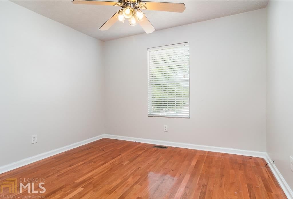 An empty room with a wooden floor and a ceiling fan, featuring a window with blinds.