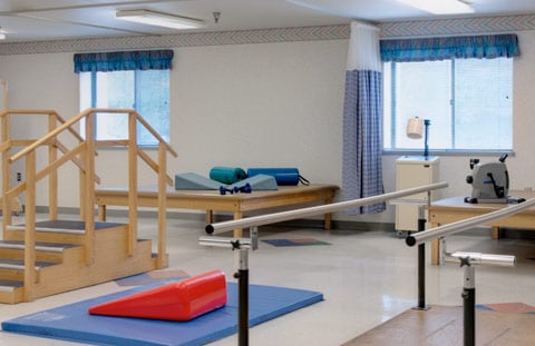 A well-equipped physical therapy room featuring exercise mats and parallel bars for rehabilitation.