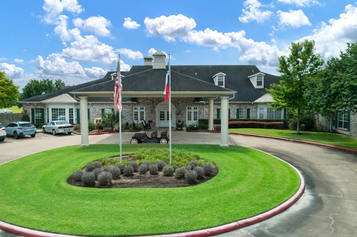 A well-maintained building with flags in front and a circular driveway surrounded by lush grass under a partly cloudy sky.