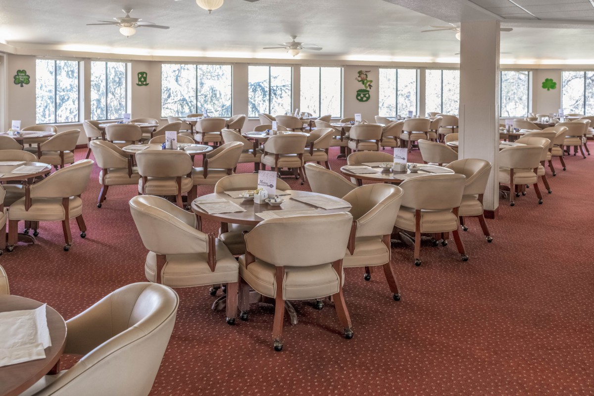 An empty dining area with round tables and cushioned chairs on a carpeted floor.