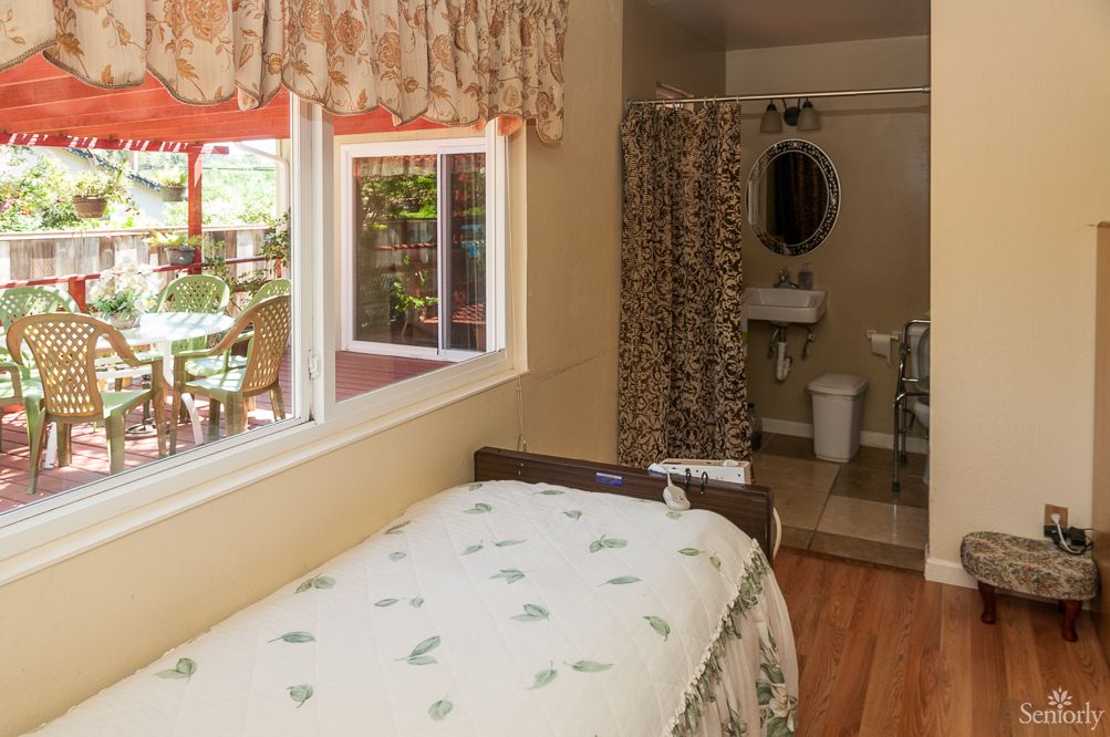 A cozy bedroom with an adjacent bathroom, featuring floral decor and a large window.