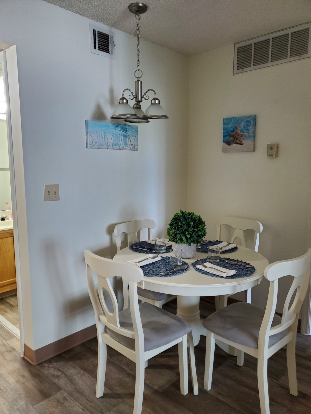A cozy dining area with a round table set for four, featuring elegant place settings and a decorative plant centerpiece.