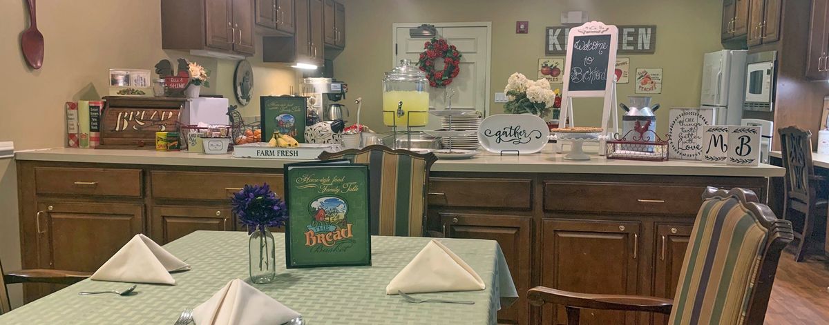 A cozy kitchen and dining area with a table set for dining, featuring a lemonade dispenser and decorative elements.