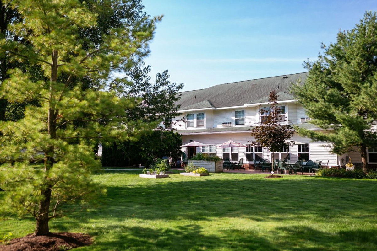 A two-story house with a large lawn and trees in the background.