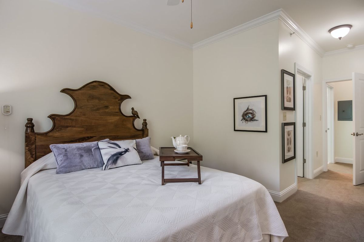 A cozy bedroom features a bed with a wooden headboard, adorned with pillows and a tea tray. Minimalist artwork decorates the walls.