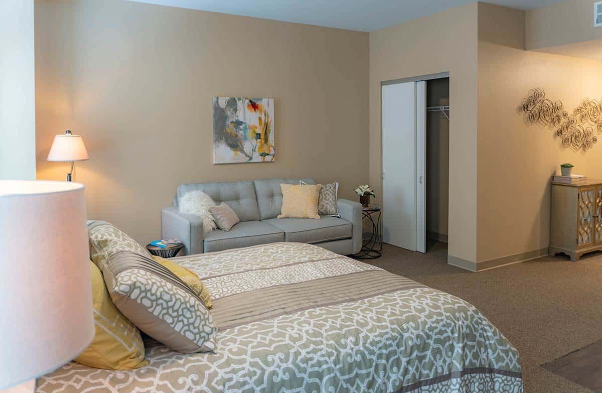 A cozy bedroom with a bed, sofa, and artwork on the wall.
