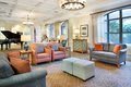A cozy and well-lit living room with comfortable sofas and chairs, featuring a chandelier and large windows.