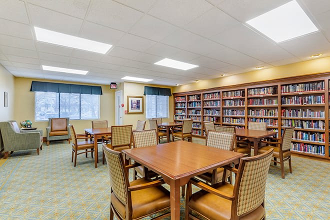 A library interior with tables and chairs, surrounded by bookshelves.