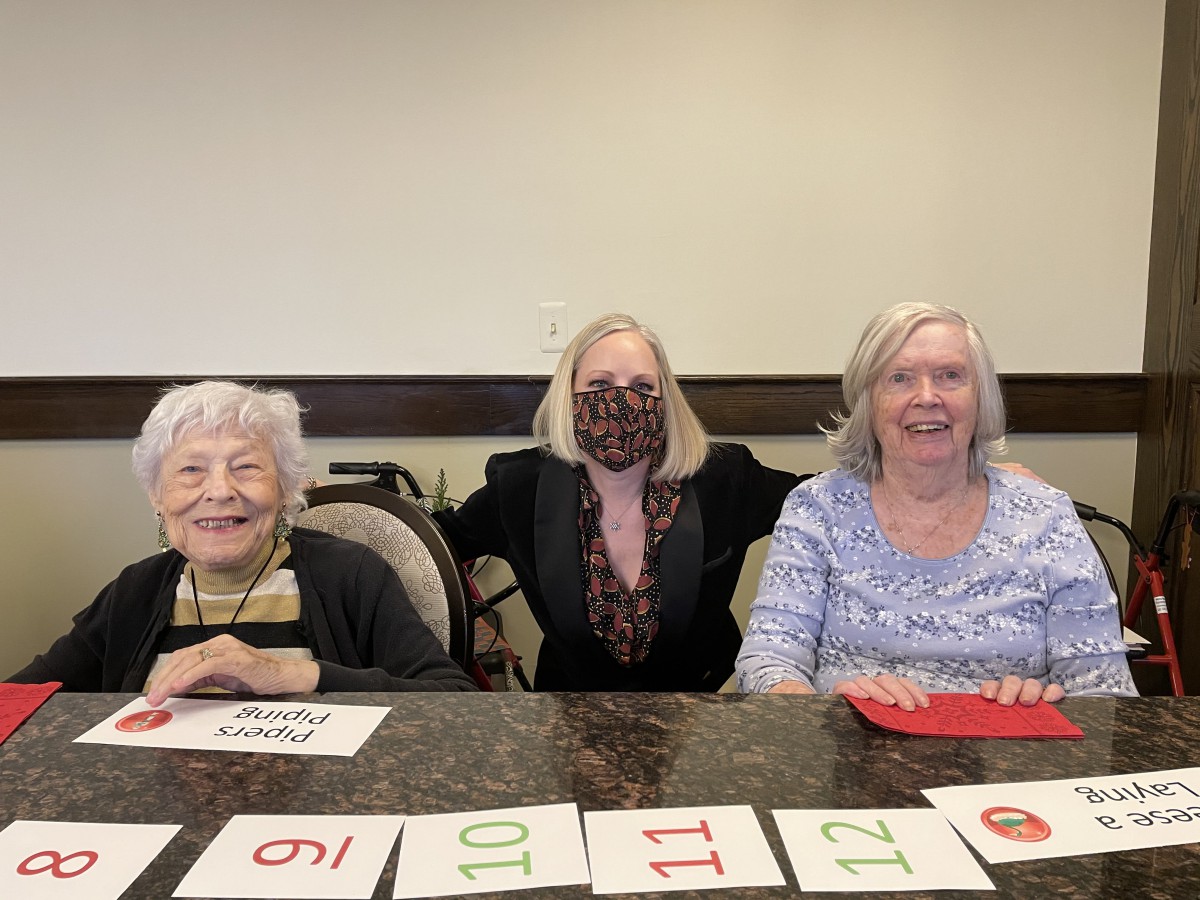A group of three women smiling while playing a card game indoors.