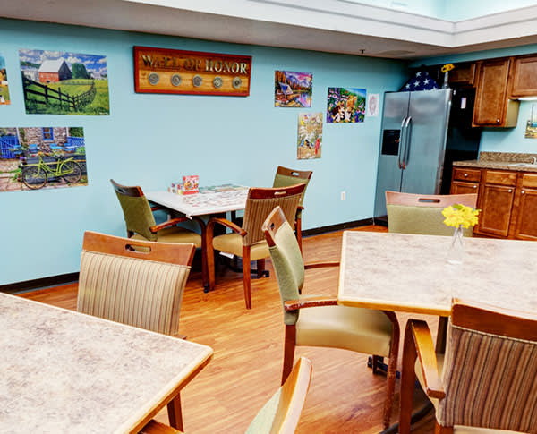 A cozy dining area featuring tables and chairs, decorated with paintings on the walls and a refrigerator in the corner.