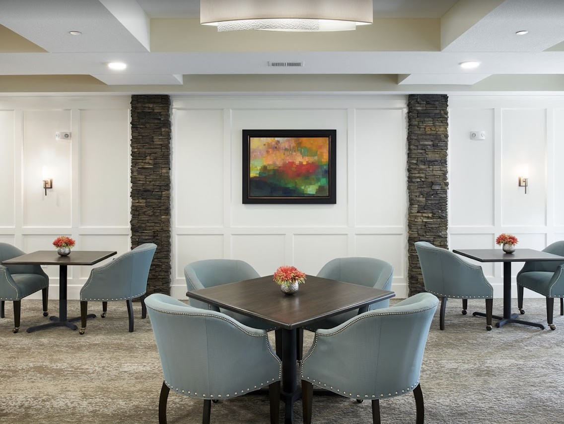A modern dining area with tables, comfortable chairs, and colorful artwork on the wall.