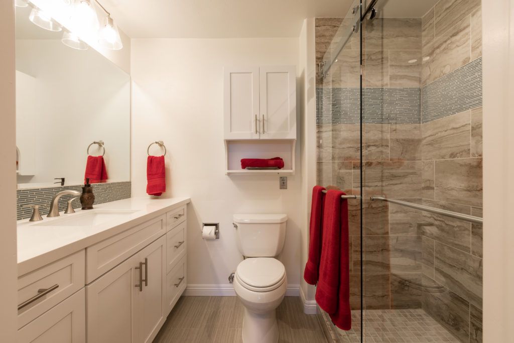 A modern bathroom with red accents, featuring a shower, toilet, and vanity.