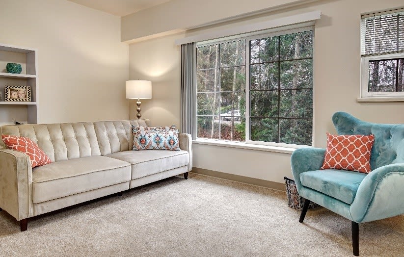 A cozy living room with a white sofa, patterned pillows, a standing lamp, and a large window.