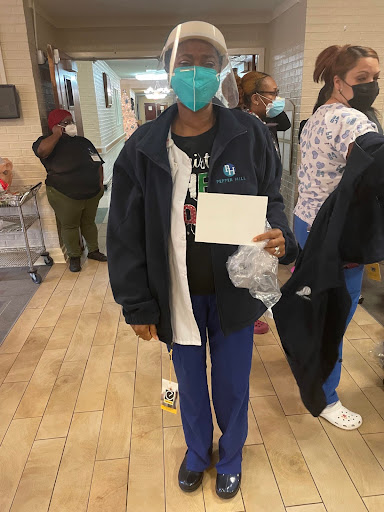 A healthcare worker in scrubs and a mask holding a card while walking down a hospital corridor.