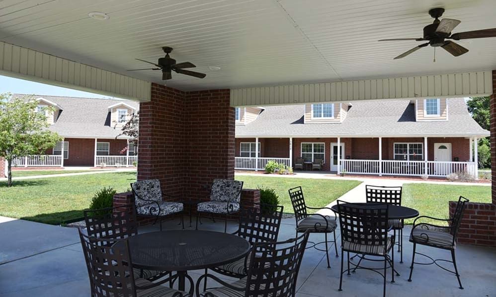 A covered outdoor patio area with tables and chairs, adjacent to a building.