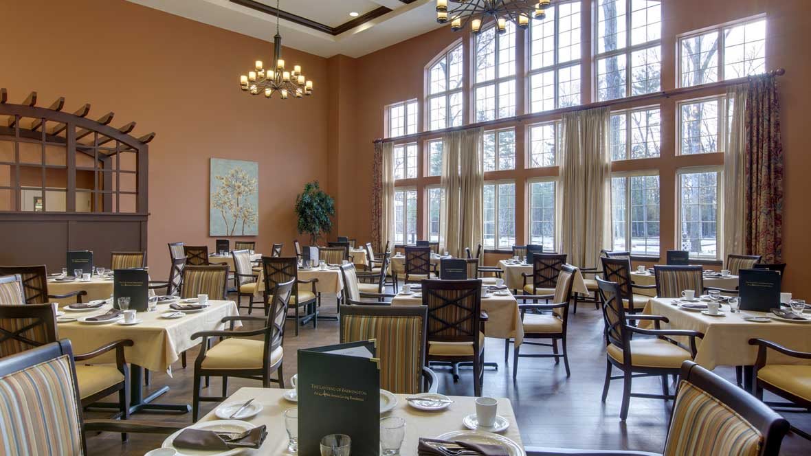 A spacious restaurant dining area with elegant tables and chairs, large windows, and a chandelier.
