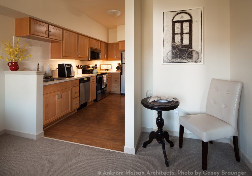 A modern apartment interior featuring a compact kitchen and cozy living area with artwork on the wall.