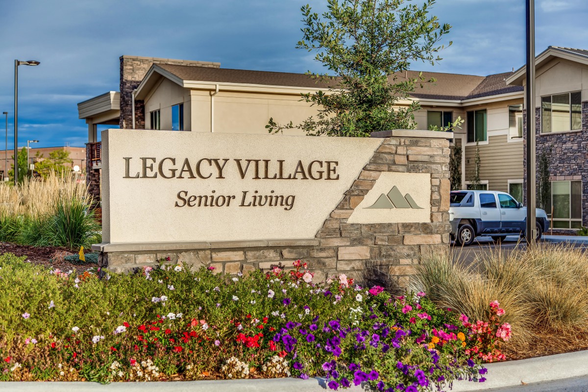 Entrance sign for Legacy Village Senior Living, surrounded by landscaped flowers.