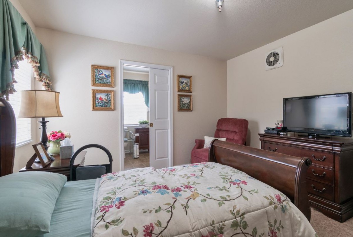 A cozy bedroom with a floral-patterned bedspread, red armchair, television, and decorative artwork on the walls.