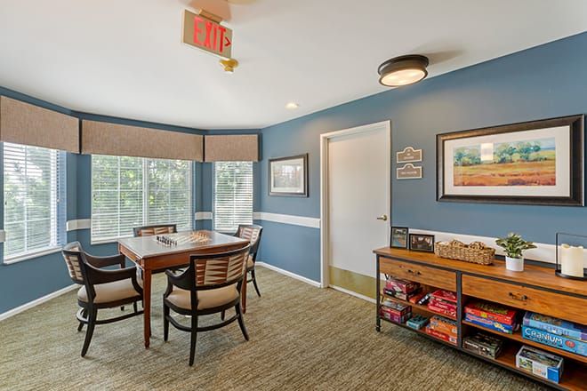 A cozy room with blue walls featuring a table and chairs, a bookshelf, and large windows.