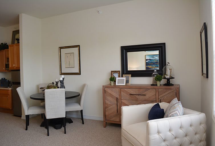 A modern living room with a dining area, featuring a wooden sideboard with a mirror above it and elegant decor elements.