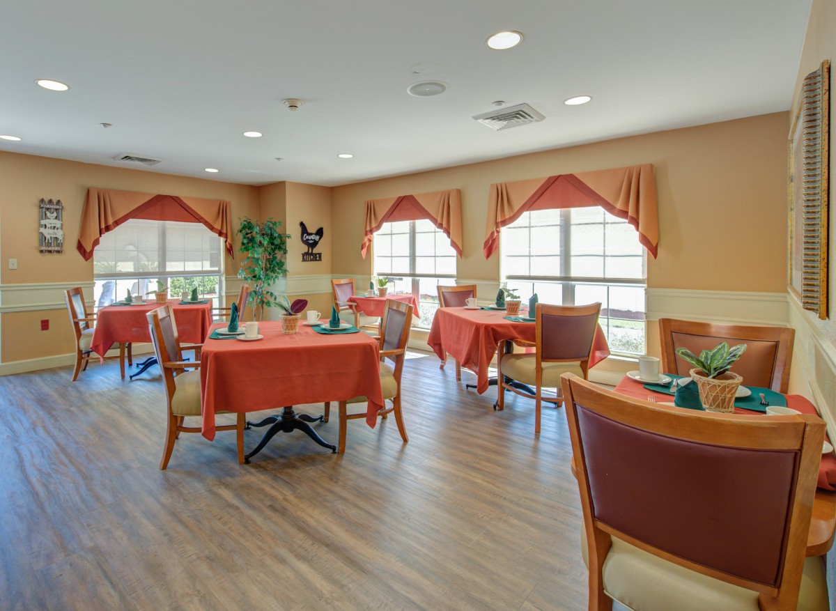 A cozy dining area with tables, chairs, and large windows adorned with curtains.