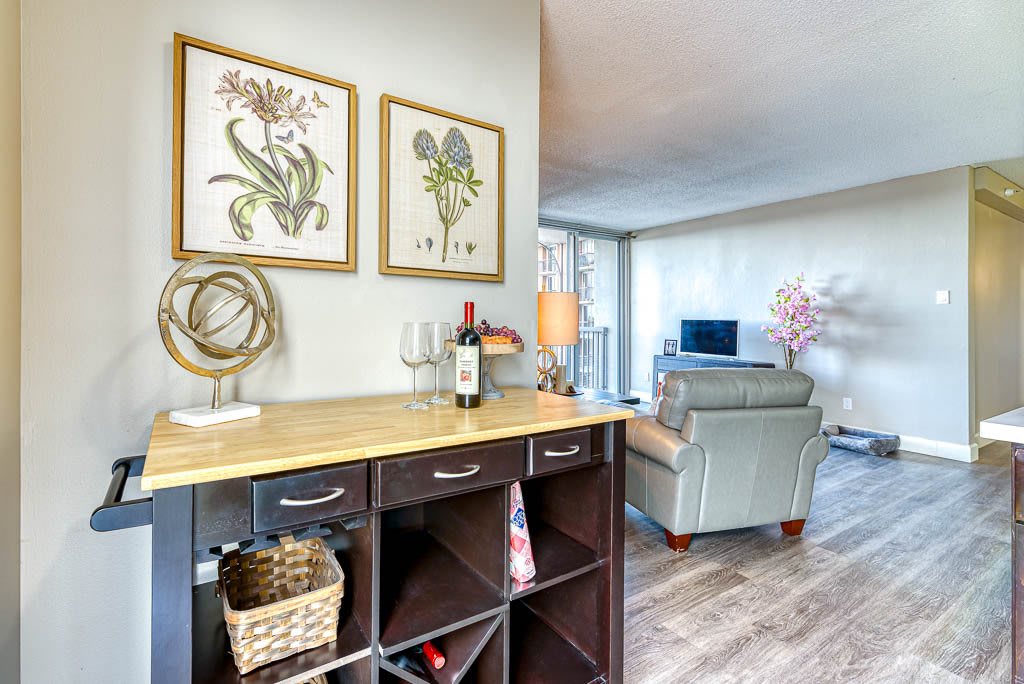 A cozy living room featuring modern decor with art prints, a wine rack, comfortable seating, and a television.
