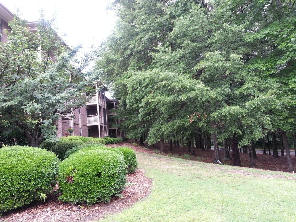 An apartment building surrounded by lush trees and well-maintained shrubbery.