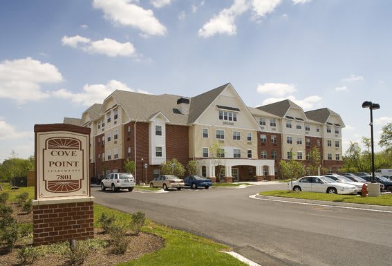 A modern residential apartment complex with a parking lot under a partly cloudy sky.