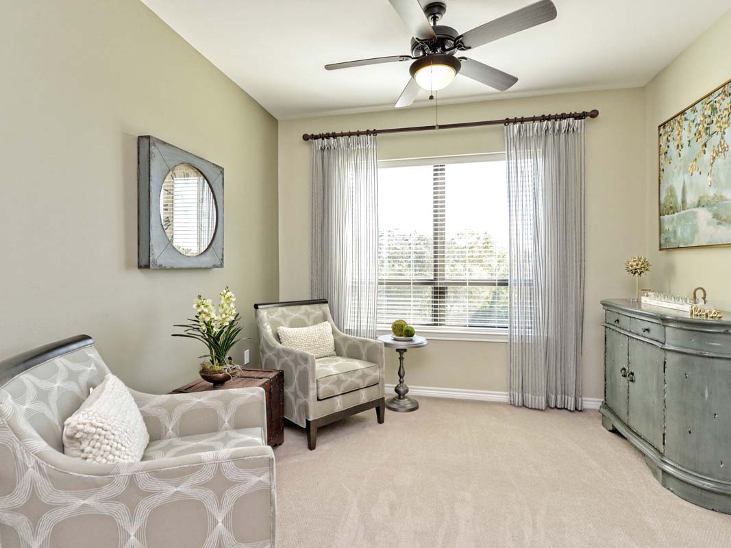 A cozy living room with an armchair, decorative plants, and a ceiling fan.