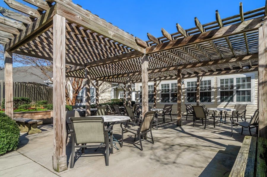 A sunny outdoor patio area with a pergola providing shade over tables and chairs.