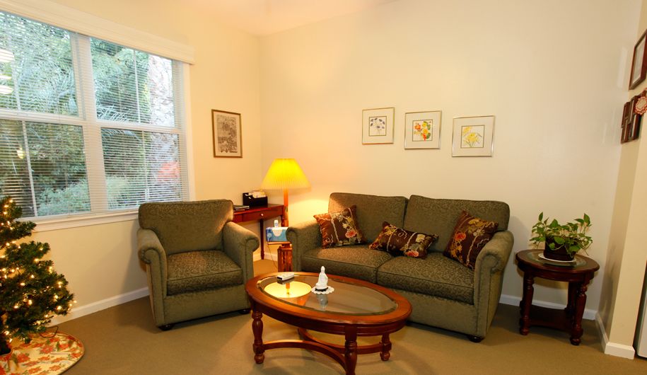 A cozy living room with a sofa, armchair, and a coffee table, softly lit by a lamp in the corner.