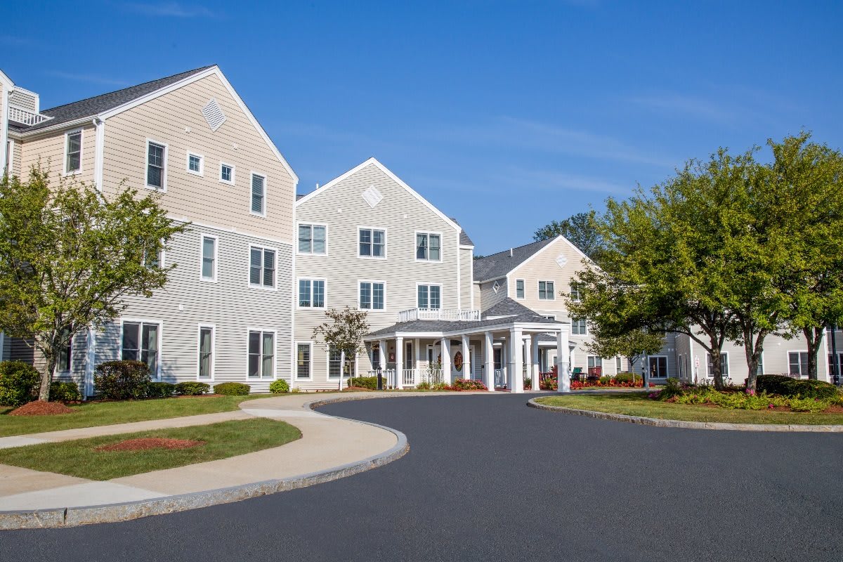 A large residential building with a driveway and landscaped surroundings under a clear blue sky.
