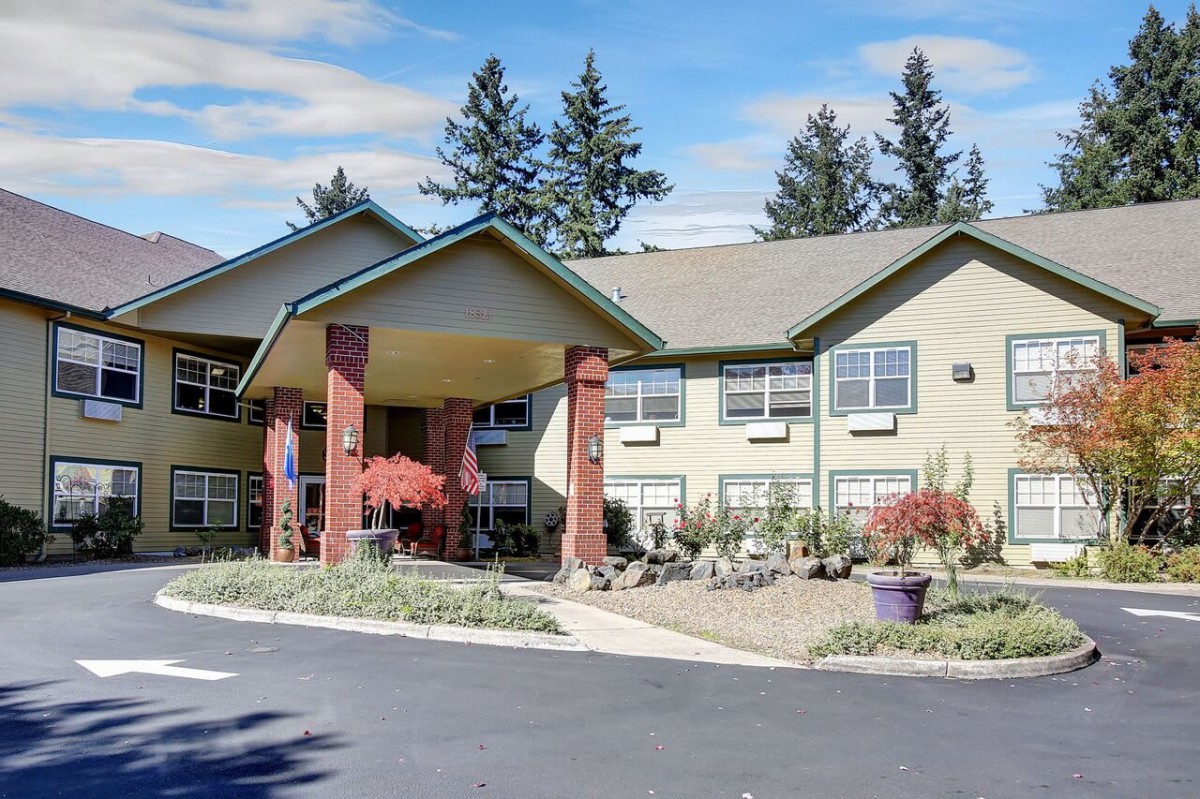 A two-story residential building with a landscaped entrance and trees in the background.